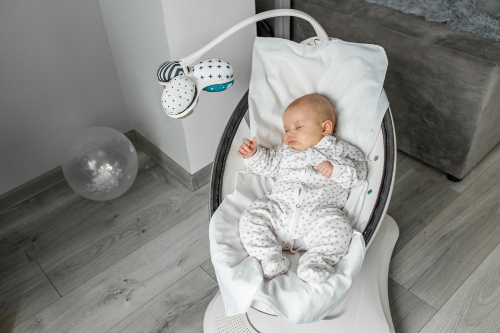 Bebe dormido en una mecedora electrica con movil de juguetes colgante